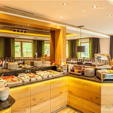 Ein einladendes Frühstücksbuffet mit einer Vielzahl von frischen Speisen und Getränken. Der Raum hat eine moderne Holz- und Glasgestaltung mit viel natürlichem Licht.