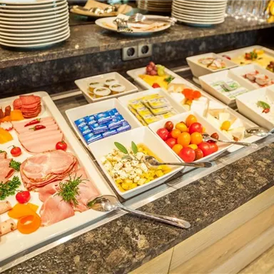 Ein reichhaltiges Buffet mit verschiedenen Wurst- und Käseplatten. Frische Tomaten, Obst und verschiedene Beilagen sind ebenfalls vorhanden.
