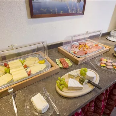 Ein Buffet mit einer Auswahl an Käse, Wurst und frischem Obst. Daneben stehen Getränke wie Saft und Gläser bereit.