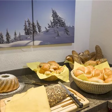 Ein Buffet mit verschiedenen Brötchen und Brot auf einem Tisch. Im Hintergrund hängt ein Bild von schneebedeckten Bäumen.