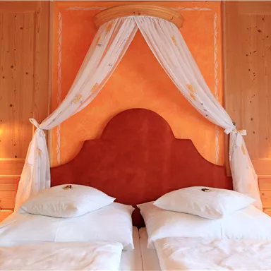 A cozy bedroom with two single beds and an orange headboard. The walls are made of wood, and soft lighting creates an inviting atmosphere.