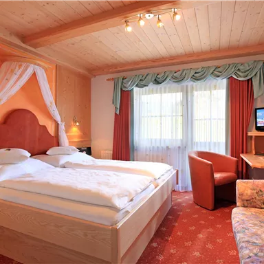 A cozy bedroom with a double bed and wooden ceiling. There is a television, a desk, and a sitting area with a DVD-like sofa.