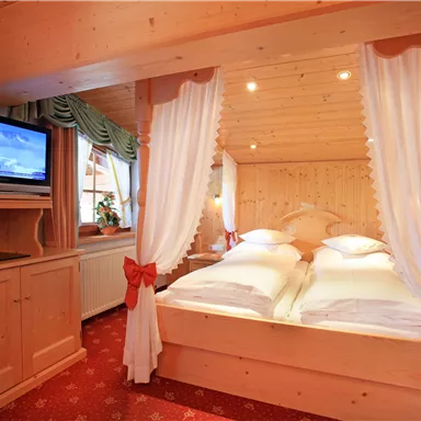 A cozy bedroom with wooden decor and a double bed. A television and small plants add extra coziness.