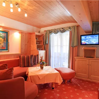 A cozy living room with red sofas and a table. A window with curtains and a television make the space inviting.