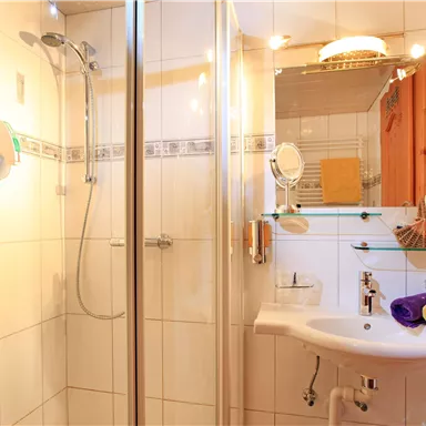 A modern bathroom with a shower and a sink. The walls are light-tiled and there are towels in various colors.