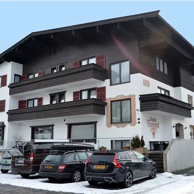 A modern building with several floors, surrounded by snow. Several cars are parked in front of the building.