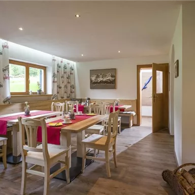 Ein einladender Essbereich mit Holztisch und Stühlen. Die Fenster lassen viel Licht herein und die gemütliche Dekoration schafft eine warme Atmosphäre.