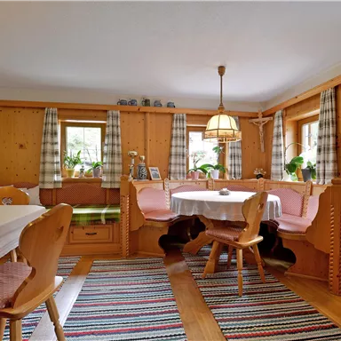 A cozy dining area with wood paneling and a large table. Many plants and traditional details create an inviting atmosphere.