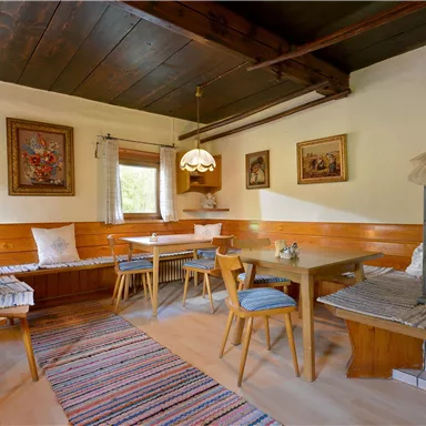 A cozy room with wooden furniture and a traditional stove. Pictures hang on the walls, and the floor is decorated with a colorful rug.