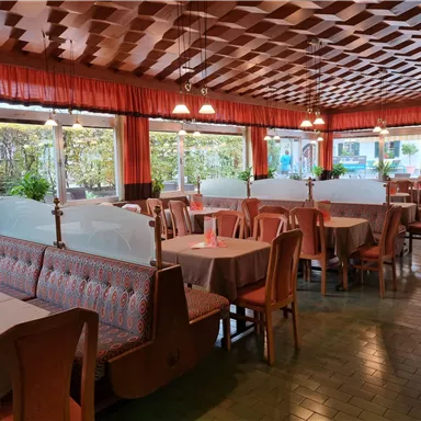 A cozy restaurant with wooden paneling and large windows. Tables are neatly set, and there are plants in the room.