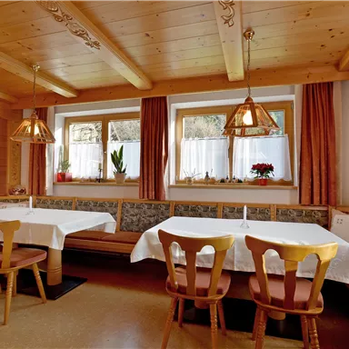 Ein gemütlicher Speisesaal mit Holzdekor und warmen Farben. Es gibt Tische mit weißen Tischdecken und Fenstern, die viel Licht hereinlassen.