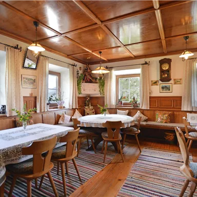 A cozy restaurant with wooden furniture and tablecloths. Large windows provide plenty of daylight and a welcoming atmosphere.