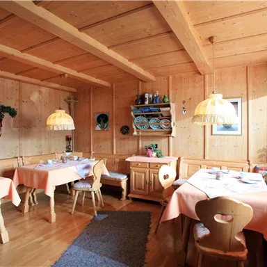 A cozy dining area with wooden walls and tables covered with pink tablecloths. The warm colors and the wood decor create an inviting atmosphere.