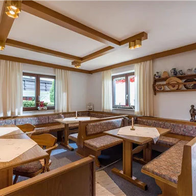 A cozy dining area with wooden tables and benches. Large windows allow plenty of light in and offer a view of the outside.