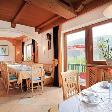 Ein gemütliches Restaurant mit Holzmöbeln und Fensterblick auf die Landschaft. Der Tisch ist schön gedeckt und Frühlingsblumen dekorieren den Raum.