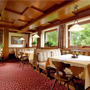 A cozy restaurant with wooden furniture and upholstered benches. The windows offer a view of the greenery and there is an inviting atmosphere.