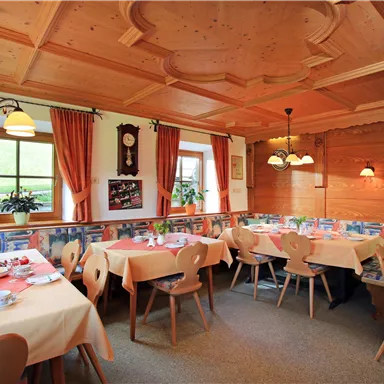 Ein gemütliches Restaurant mit Holzelementen und warmen Farben. Die Tische sind festlich gedeckt und der Raum strahlt eine einladende Atmosphäre aus.