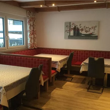 Ein gemütliches Restaurant mit Holztischen und roten Sitzbänken. An den Wänden hängen dekorative Bilder und die Fenster lassen viel Licht herein.