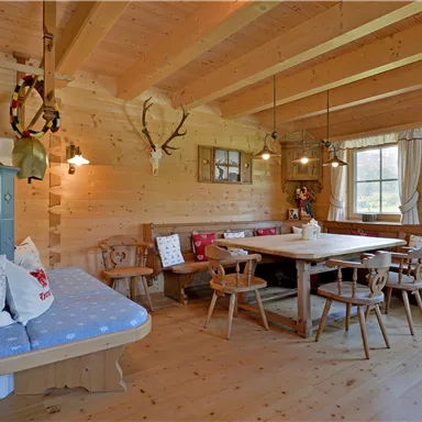 Ein gemütlicher Raum mit Holzwänden und einem großen Esstisch. Der Raum ist rustikal eingerichtet und verfügt über eine Bank und verschiedene Sitze.
