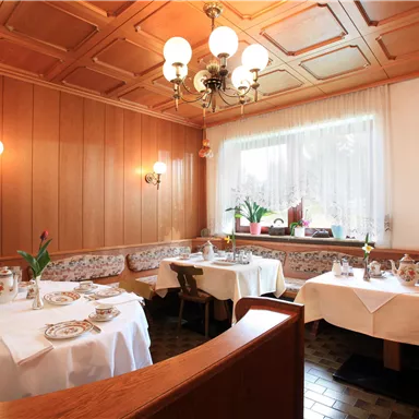 Ein gemütliches Restaurant mit Holzwänden und eleganter Tischdekoration. Es gibt weiße Tischdecken und eine angenehme Atmosphäre.