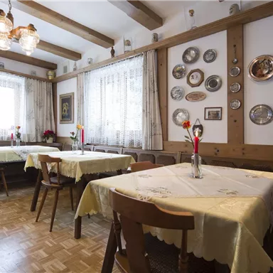 Ein gemütliches Restaurant mit Holzmöbeln und dekorativen Tellern an den Wänden. Die Tische sind mit weißen Tischtüchern eingedeckt und jeweils mit einer Blume geschmückt.