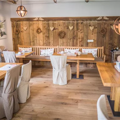 Ein gemütliches Restaurant mit Holztischen und -bänken. Warmes Licht und eine rustikale Holzdecke schaffen eine angenehme Atmosphäre.