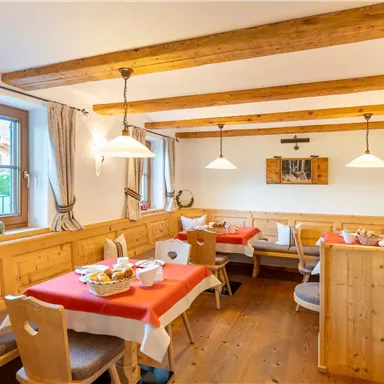 A cozy dining area with wooden furniture and red tablecloths. Large windows let in plenty of light and create an inviting atmosphere.