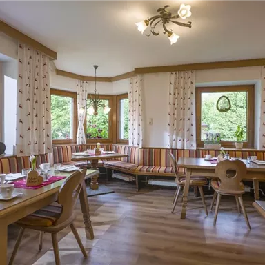 Ein gemütliches Restaurant mit Holztischen und bunt gestreiften Bänken. Die Fenster bieten einen Blick ins Freie und lassen viel Tageslicht herein.