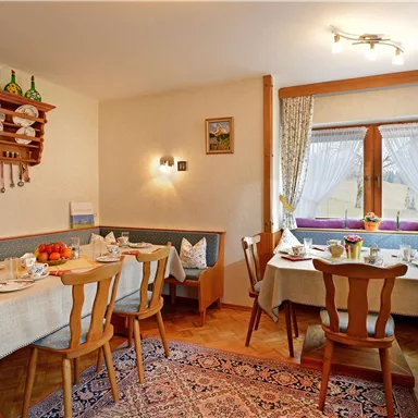 Ein gemütlicher Essbereich mit Holzmöbeln und einem Tisch, der für das Frühstück gedeckt ist. Helle Fenster bieten einen schönen Blick nach draußen und verleihen dem Raum eine einladende Atmosphäre.