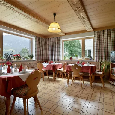 Ein gemütlicher Essbereich mit Tischen und Stühlen. Große Fenster bieten einen Ausblick auf die Berge und viel Tageslicht.