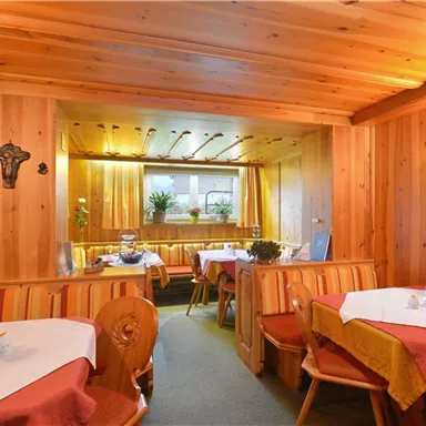 A cozy restaurant with wooden paneling and warm lighting. The tables are neatly set, and there are plants in the background.