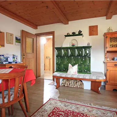 A cozy room with wooden furniture and a traditional stove. The table is set with red and white checkered tablecloths.