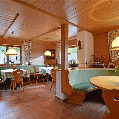 A cozy restaurant area with wooden furniture and green tables. The windows let in plenty of daylight and create an inviting atmosphere.