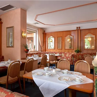 Ein gemütliches Restaurant mit Holzmöbeln und Tischgedeck. Der Raum ist freundlich gestaltet, mit dekorativen Spiegeln und Pflanzen.