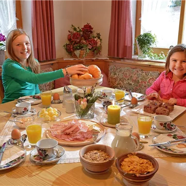 Ein fröhliches Frühstück mit zwei Kindern an einem gedeckten Tisch. Der Tisch ist voller frischer Speisen und Getränke, darunter Obst, Eier und Säfte.