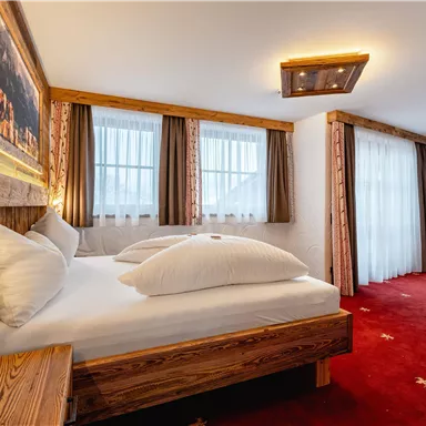 Ein gemütliches Schlafzimmer mit einem Holzrahmenbett und weißen Kissen. Große Fenster sorgen für viel Licht und eine einladende Atmosphäre.