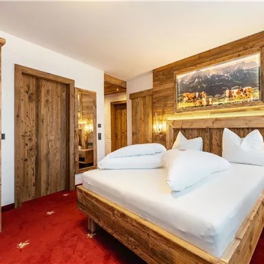 Ein gemütliches Schlafzimmer mit Holzmöbeln und roten Teppich. Die Wände sind mit warmen Holzelementen und einem Landschaftsbild dekoriert.