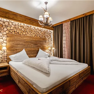 Ein gemütliches Schlafzimmer mit einem Holzbett und hellen Kissen. Die Wand ist mit Holzscheiten dekoriert und es gibt stimmungsvolle Beleuchtung.