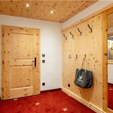 Ein heller Flur mit Holzwänden und einer roten Teppichboden. An der Wand hängen mehrere K hooks und eine Tasche ist sichtbar.