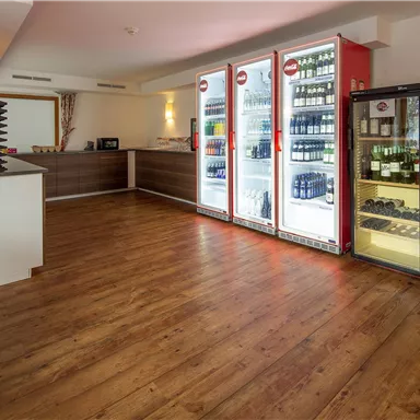Ein modern gestalteter Raum mit einem Holzfußboden und einem Empfangsbereich. Kühlschränke mit Getränken und Snacks stehen an der Wand.