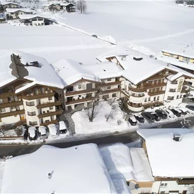 Eine Winterlandschaft mit schneebedeckten Gebäuden und angrenzenden Straßen. Die Szene wirkt friedlich und einladend unter dem weißen Schnee.