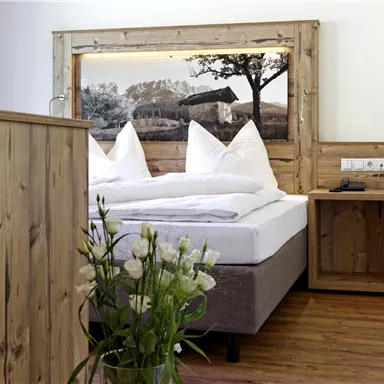 Ein modernes Schlafzimmer mit Holzdekor und einem großen Bett. Auf einem Nachttisch steht eine Vase mit frischen Blumen.