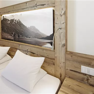 Ein elegantes Schlafzimmer mit zwei Betten und weißen Kissen. Im Hintergrund ist ein Bild von einer Berglandschaft zu sehen.