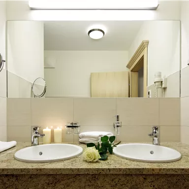 Ein modernes Badezimmer mit einem Doppelwaschbecken aus Granit. Auf der Ablage stehen Kerzen und eine Rose, die eine entspannende Atmosphäre schaffen.