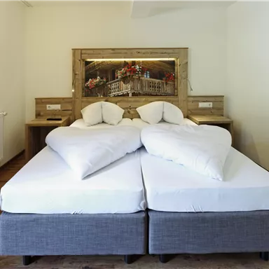 Ein gemütliches Schlafzimmer mit einem Doppelbett und hellen, neutralen Farben. Im Hintergrund ist ein schönes Landschaftsbild zu sehen.