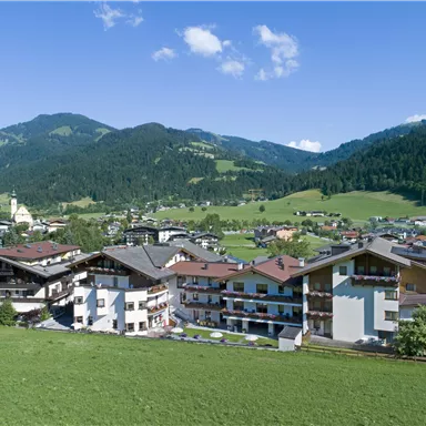Eine malerische Berglandschaft mit traditionellen Gebäuden und grünen Wiesen. Im Hintergrund sind majestätische Berge und ein klarer blauer Himmel zu sehen.