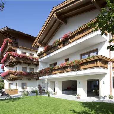 Ein malerisches Gebäude mit Balkonen, die mit blühenden Pflanzen geschmückt sind. Der grüne Rasen und der klare Himmel verleihen der Szene eine einladende Atmosphäre.