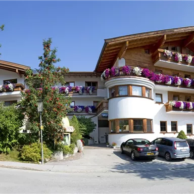 Ein malerisches Hotel mit Balkonen, die mit bunten Blumen dekoriert sind. Umgeben von Bäumen und einem klaren blauen Himmel.