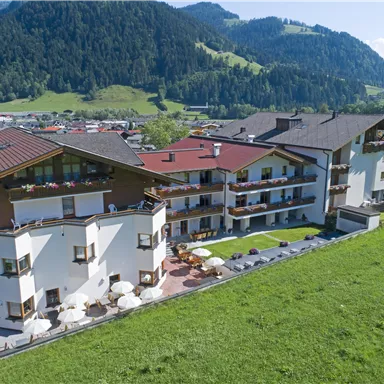 Ein modernes Hotelgebäude umgeben von einer schönen grünen Landschaft. Im Hintergrund sind sanfte Berge und ein klarer Himmel zu sehen.