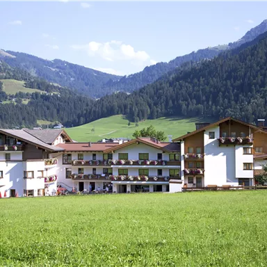 Ein malerisches Hotelgebäude in den Alpen mit grünen Wiesen und Bergen im Hintergrund. Der Himmel ist klar und die Umgebung ist ruhig und einladend.